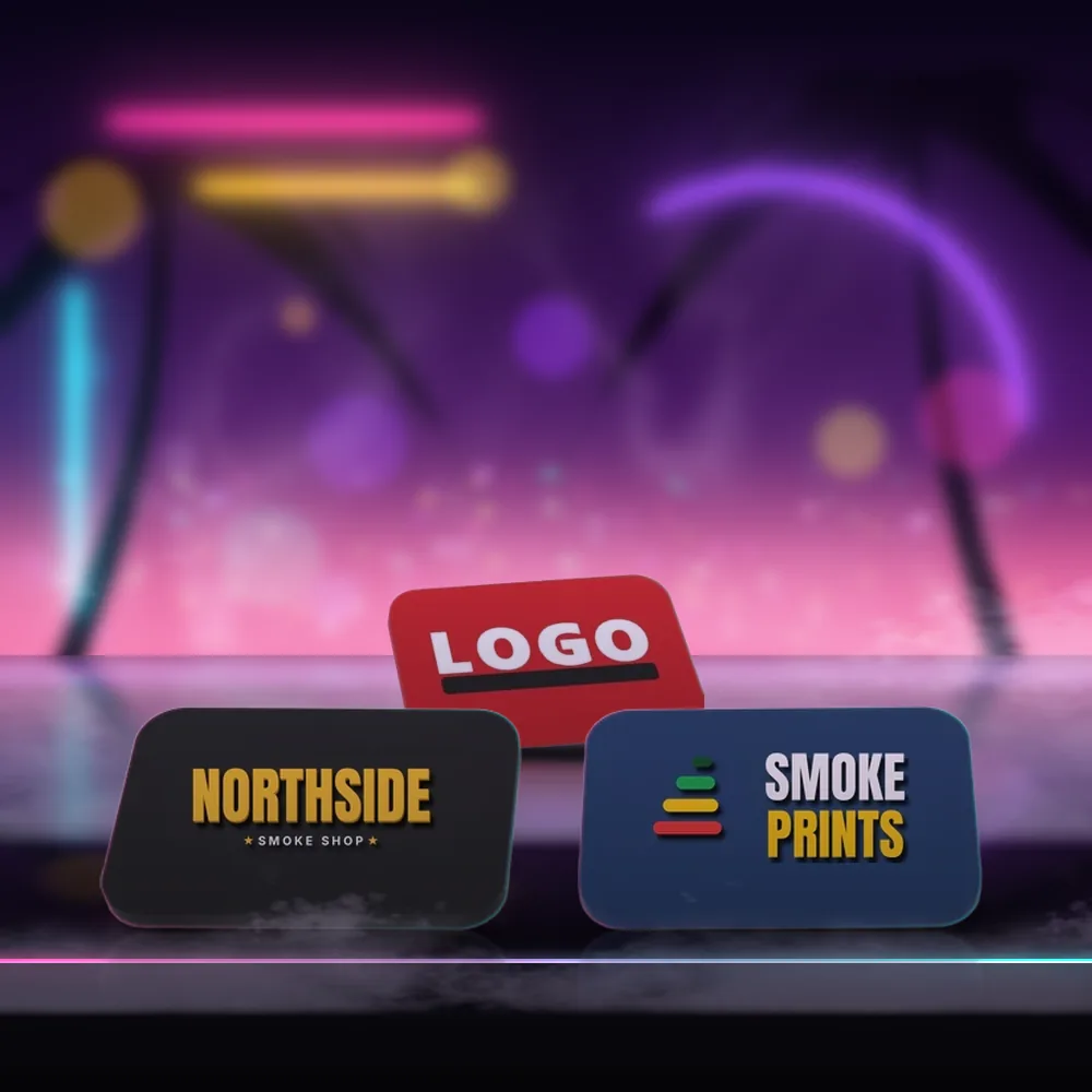 Tres imanes de nevera sobre un mostrador con luz de neón: uno negro con un logo de muestra de NORTHSIDE SMOKE SHOP, uno azul marino con el logo de Smoke Prints y uno rojo con LOGO